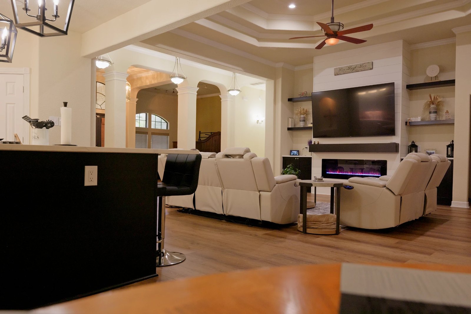 Open-concept living area with a shiplap fireplace wall, built-in shelving, wood-look flooring and arched entryways